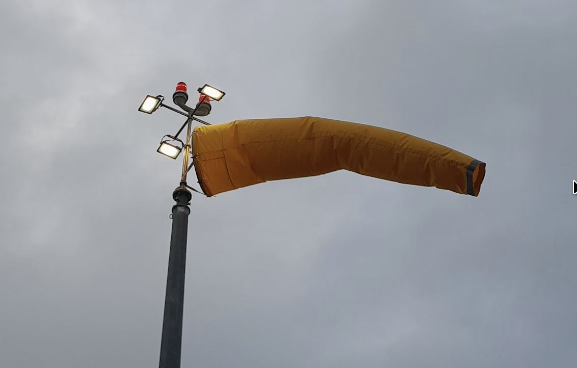 Lighted Windsock mounted on a light tower at an industrial airfield, giving instant wind direction and speed data